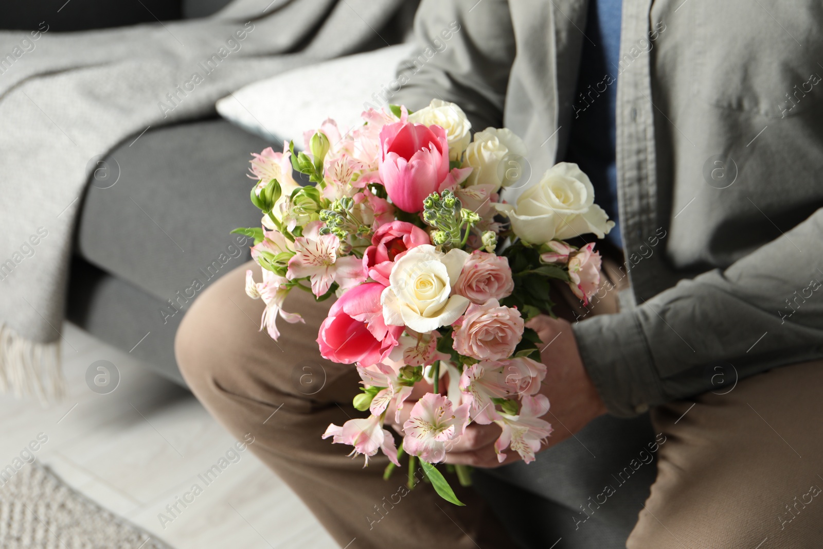 Photo of Man holding bouquet of beautiful flowers indoors, closeup