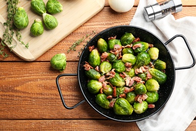 Photo of Flat lay composition of tasty roasted Brussels sprouts with bacon on wooden table