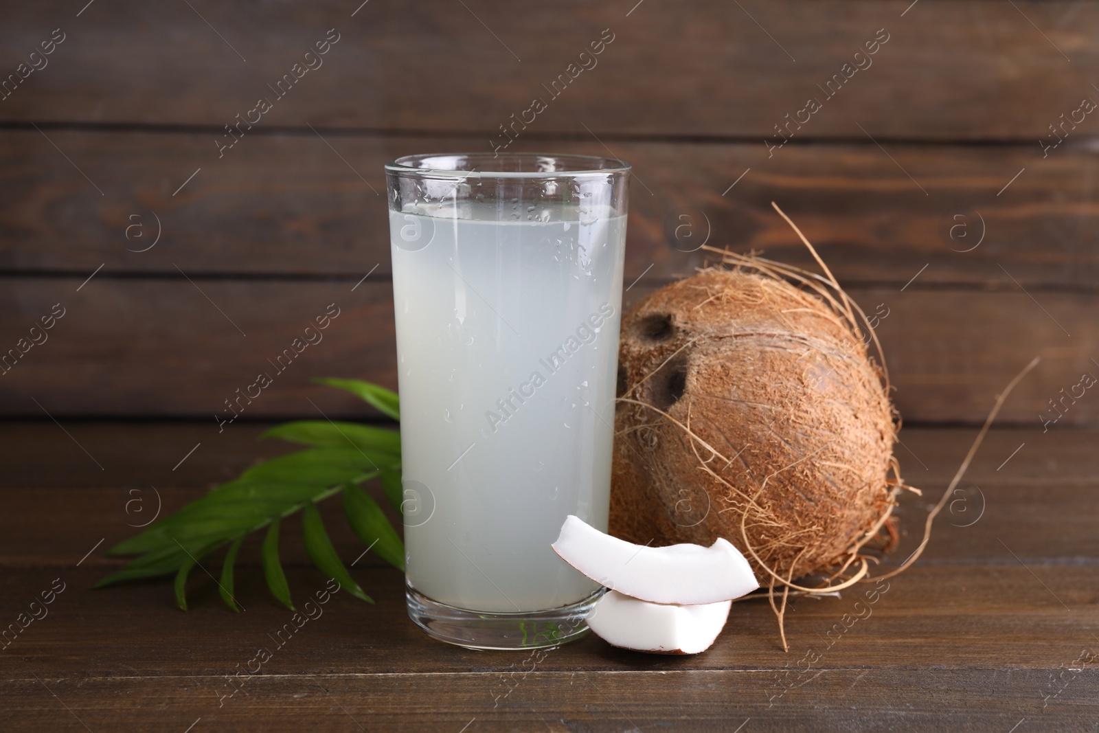 Photo of Glass of coconut water, leaf and nuts on wooden table