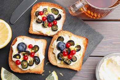 Photo of Tasty sandwiches with cream cheese, blueberries, red currants and lemon zest near cup of tea on wooden table, flat lay