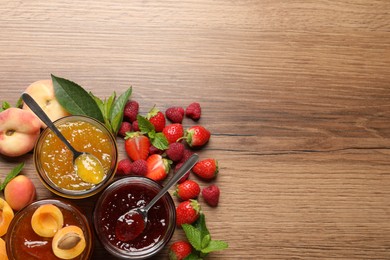Photo of Jars with different jams and fresh fruits on wooden table, flat lay. Space for text