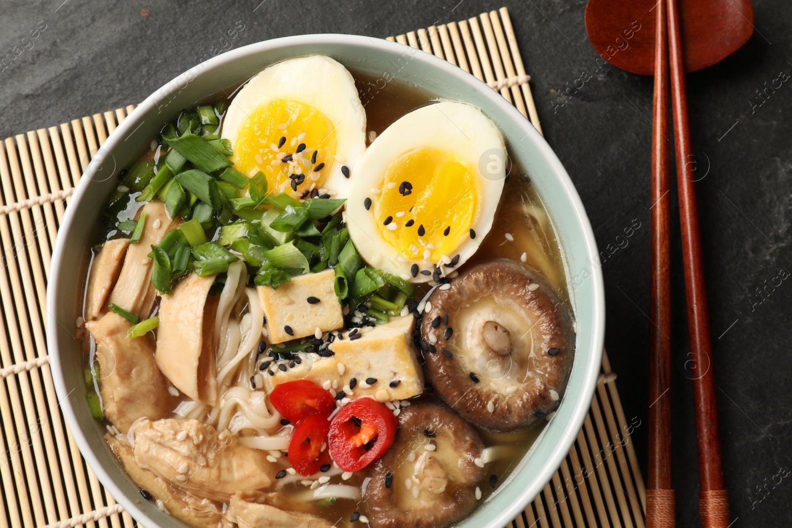 Photo of Noodle soup. Bowl of delicious ramen, ingredients and chopsticks on black table, top view