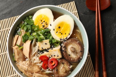 Photo of Noodle soup. Bowl of delicious ramen, ingredients and chopsticks on black table, top view