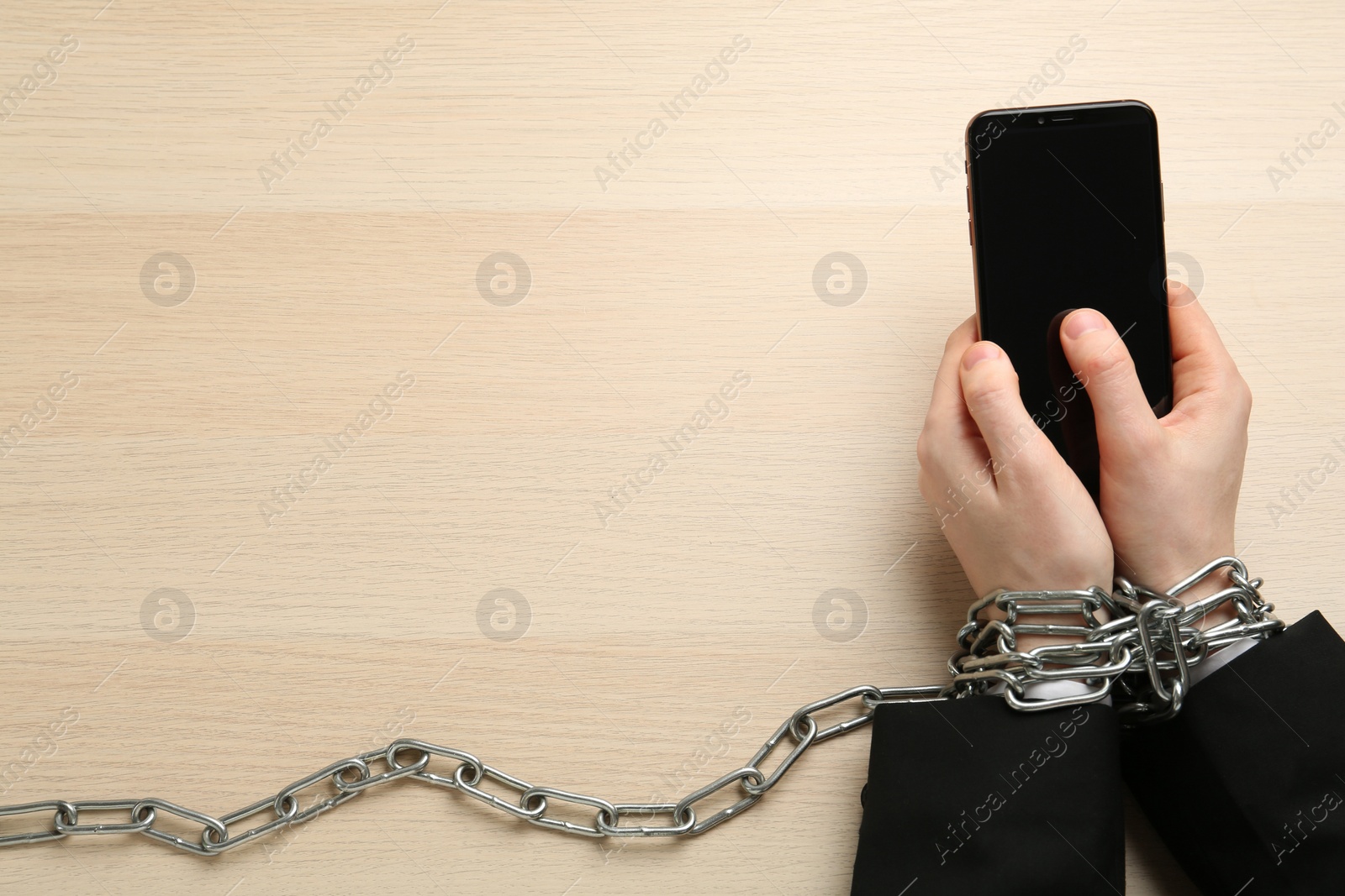 Photo of Man holding smartphone in chained hands at wooden table, top view. Internet addiction