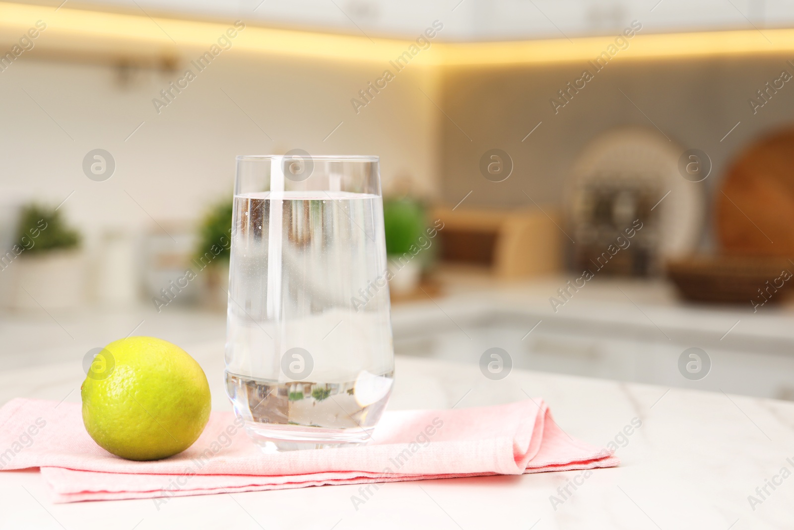 Photo of Filtered water in glass and lime on white marble table in kitchen, closeup. Space for text