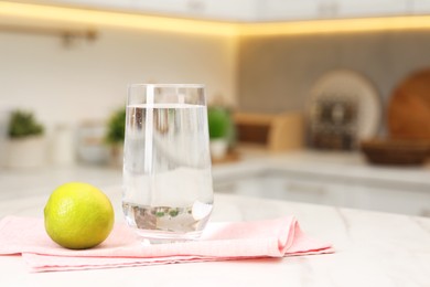 Photo of Filtered water in glass and lime on white marble table in kitchen, closeup. Space for text