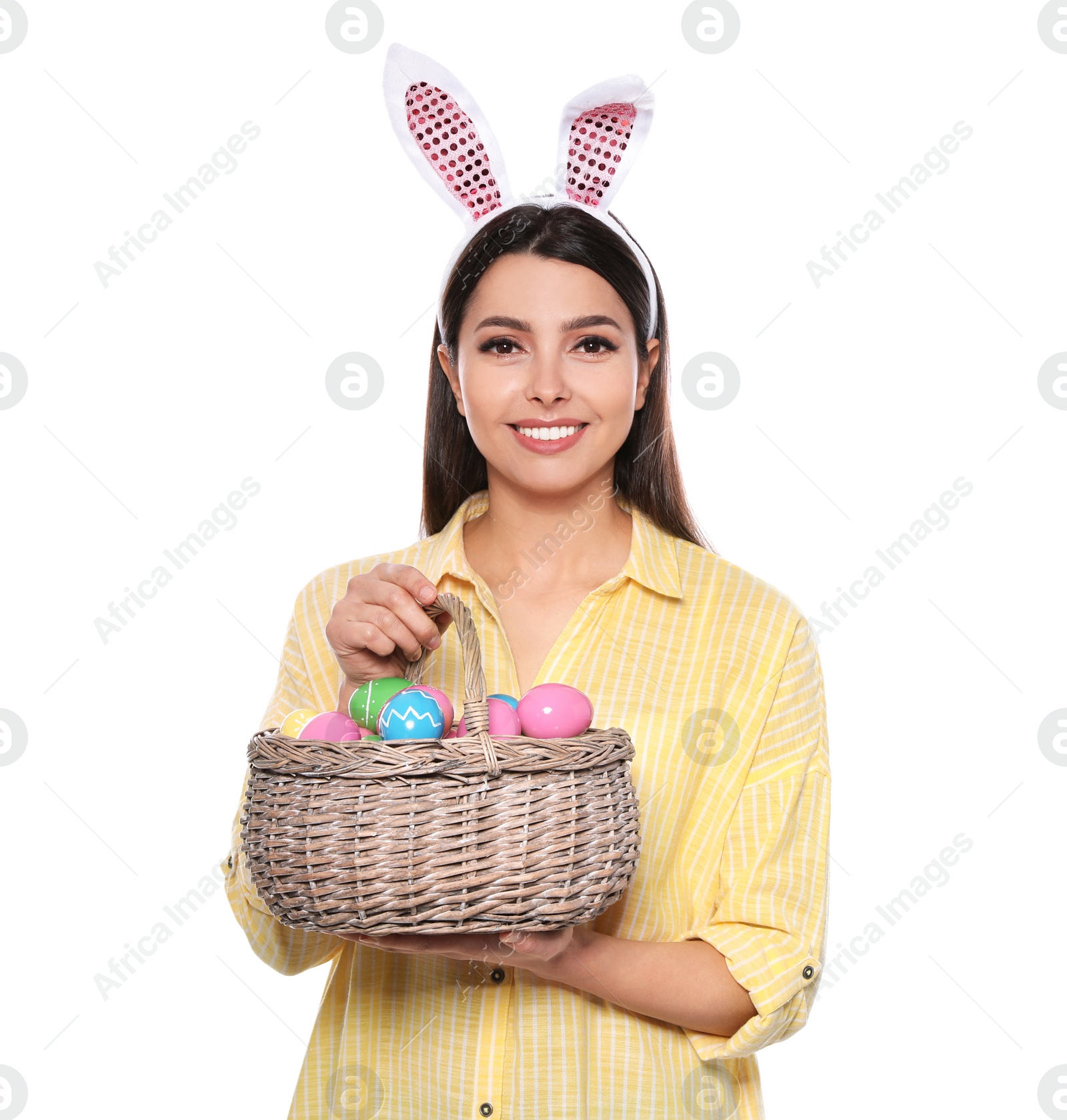 Photo of Beautiful woman in bunny ears headband holding basket with Easter eggs on white background