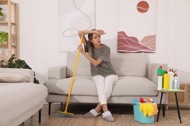 Tired young mother sitting on sofa in messy living room