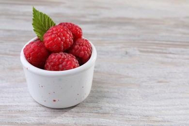 Photo of Tasty ripe raspberries and green leaf on white wooden table, space for text
