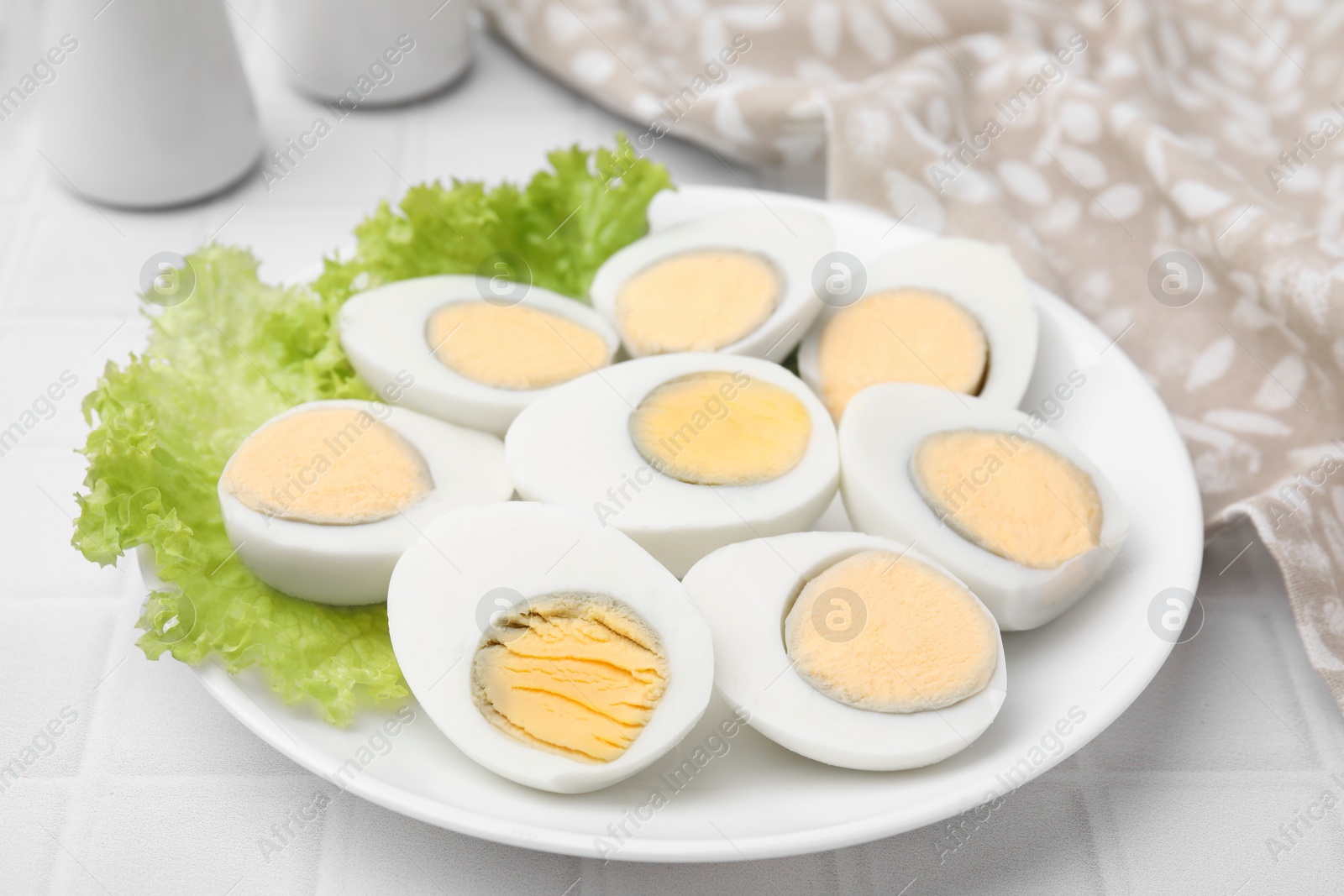 Photo of Fresh hard boiled eggs and lettuce on white tiled table