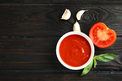 Photo of Flat lay composition with bowl of tomato sauce on wooden table. Space for text