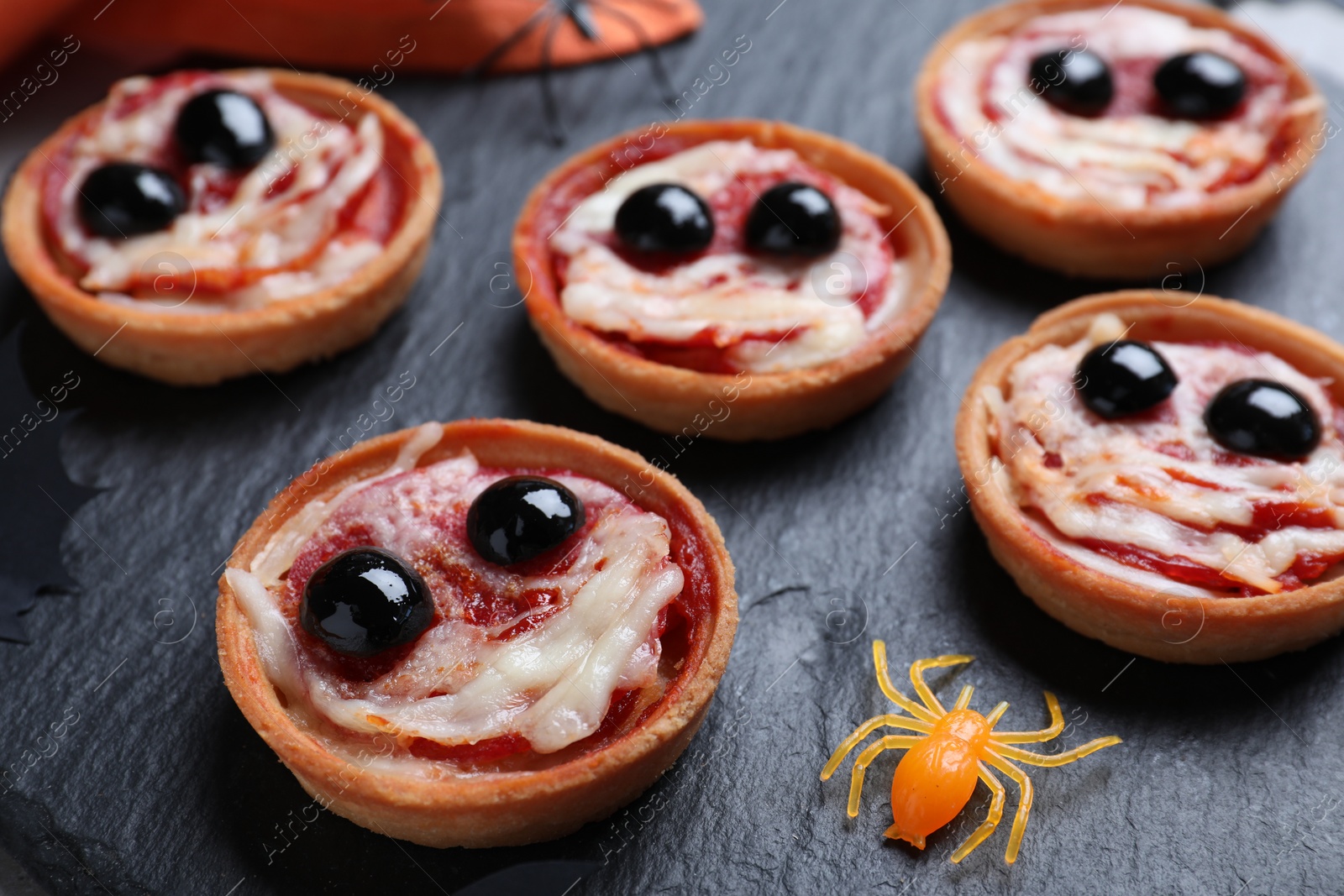 Photo of Cute monster tartlets served on slate plate, closeup. Halloween party food