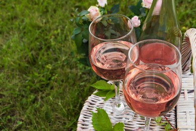 Photo of Glasses and bottle of delicious rose wine on picnic basket outdoors, closeup. Space for text