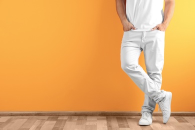 Photo of Young man in stylish jeans near color wall with space for text, focus on legs