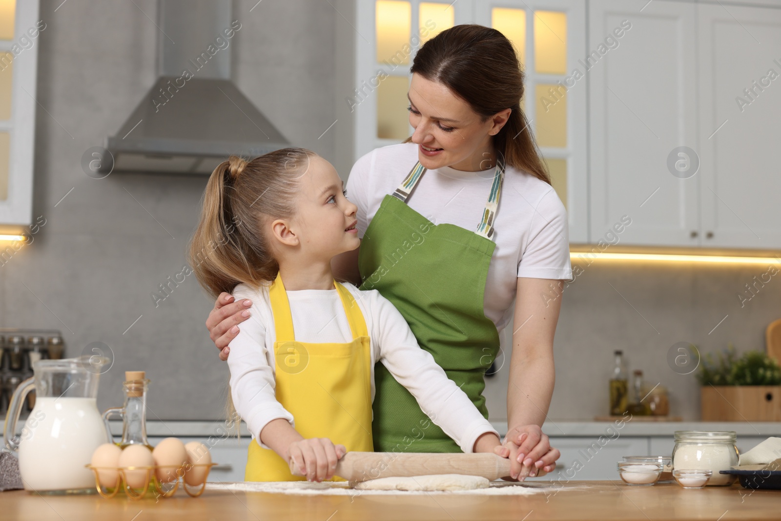 Photo of Making bread. Mother and her daughter rolling dough at wooden table in kitchen