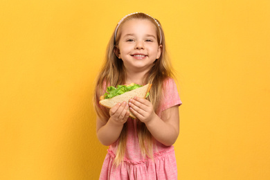 Cute little girl with tasty sandwich on yellow background