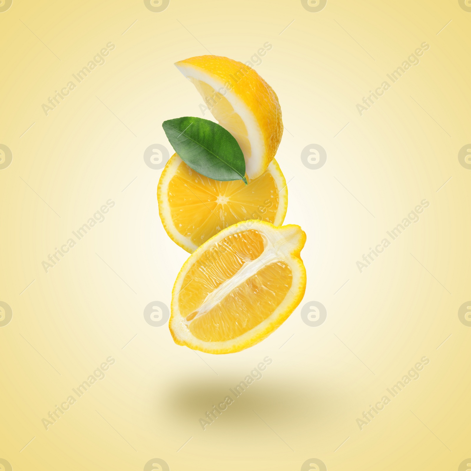 Image of Cut fresh lemons with green leaf falling on pastel gold background