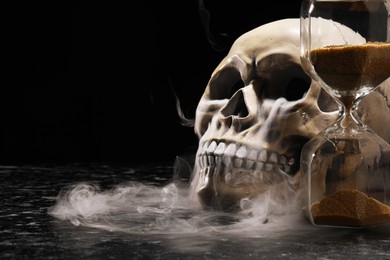 Photo of Human skull, hourglass and smoke on black background. Space for text