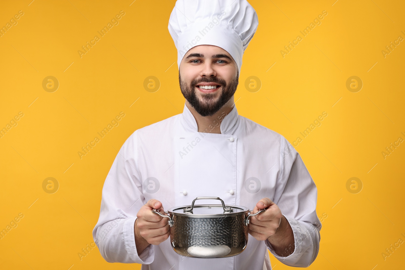 Photo of Happy young chef in uniform holding cooking pot on orange background