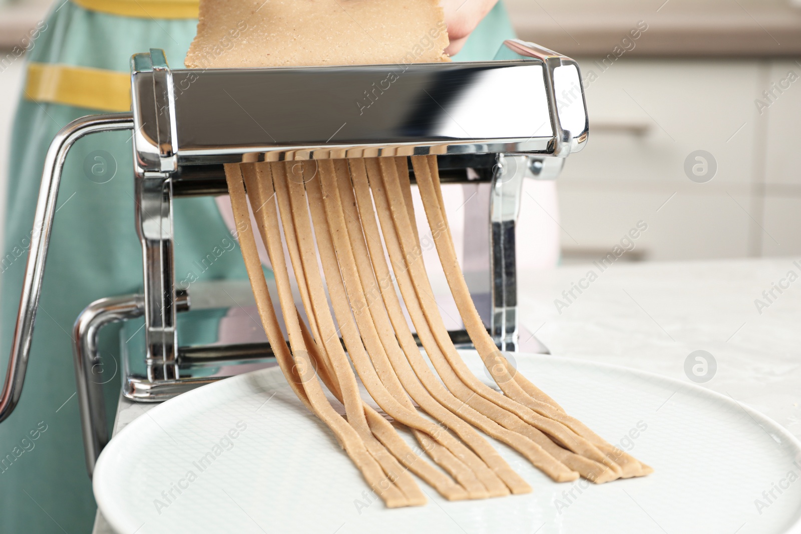 Photo of Woman preparing soba (buckwheat noodles) with pasta maker machine in kitchen, closeup