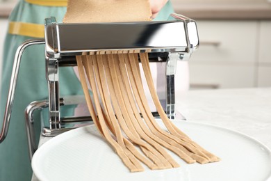 Photo of Woman preparing soba (buckwheat noodles) with pasta maker machine in kitchen, closeup