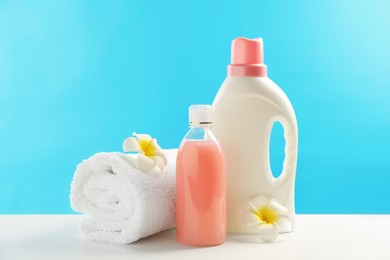 Photo of Bottles of laundry detergents, towel and plumeria flowers on white table