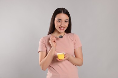 Portrait of happy woman with tasty yogurt on grey background