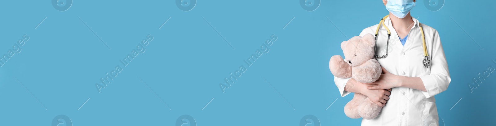 Photo of Pediatrician with teddy bear and stethoscope on light blue background, closeup