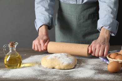 Photo of Woman rolling raw dough at wooden table, closeup