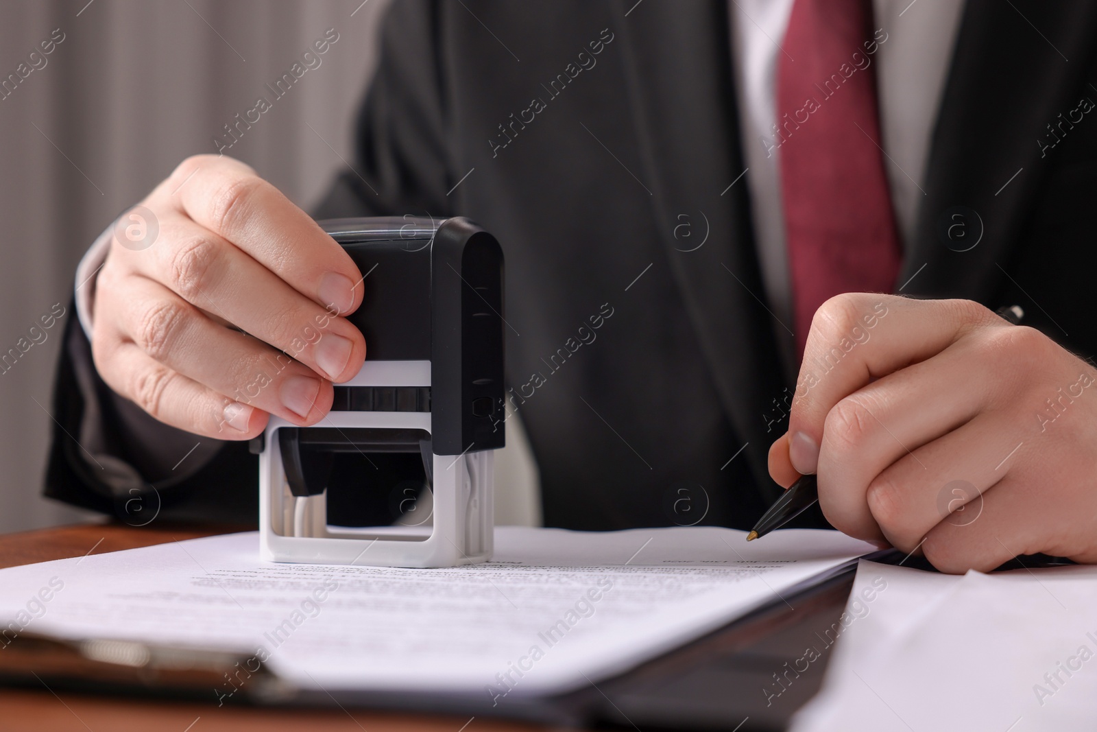 Photo of Notary with pen stamping document at table in office, closeup