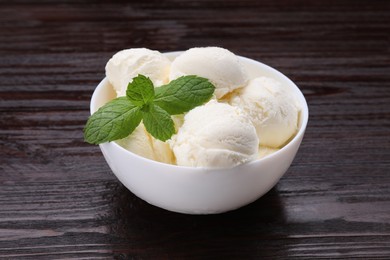 Photo of Delicious vanilla ice cream and mint in bowl on wooden table, closeup