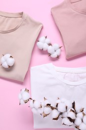 Cotton branch with fluffy flowers and t-shirts on pink background, flat lay