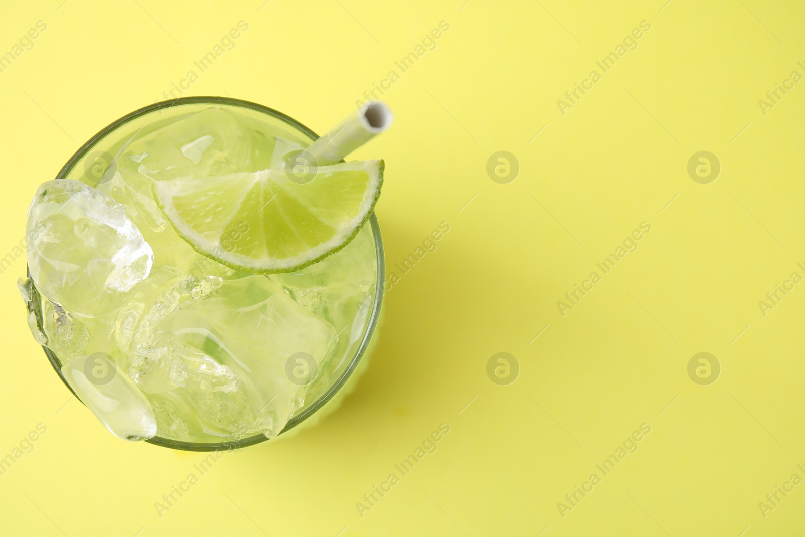 Photo of Glass of refreshing drink with lime on yellow background, top view. Space for text