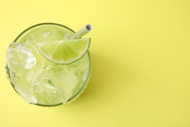 Glass of refreshing drink with lime on yellow background, top view. Space for text
