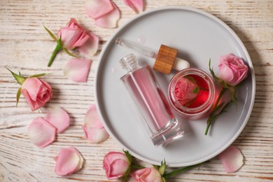 Flat lay composition with essential rose oil and flowers on white wooden table