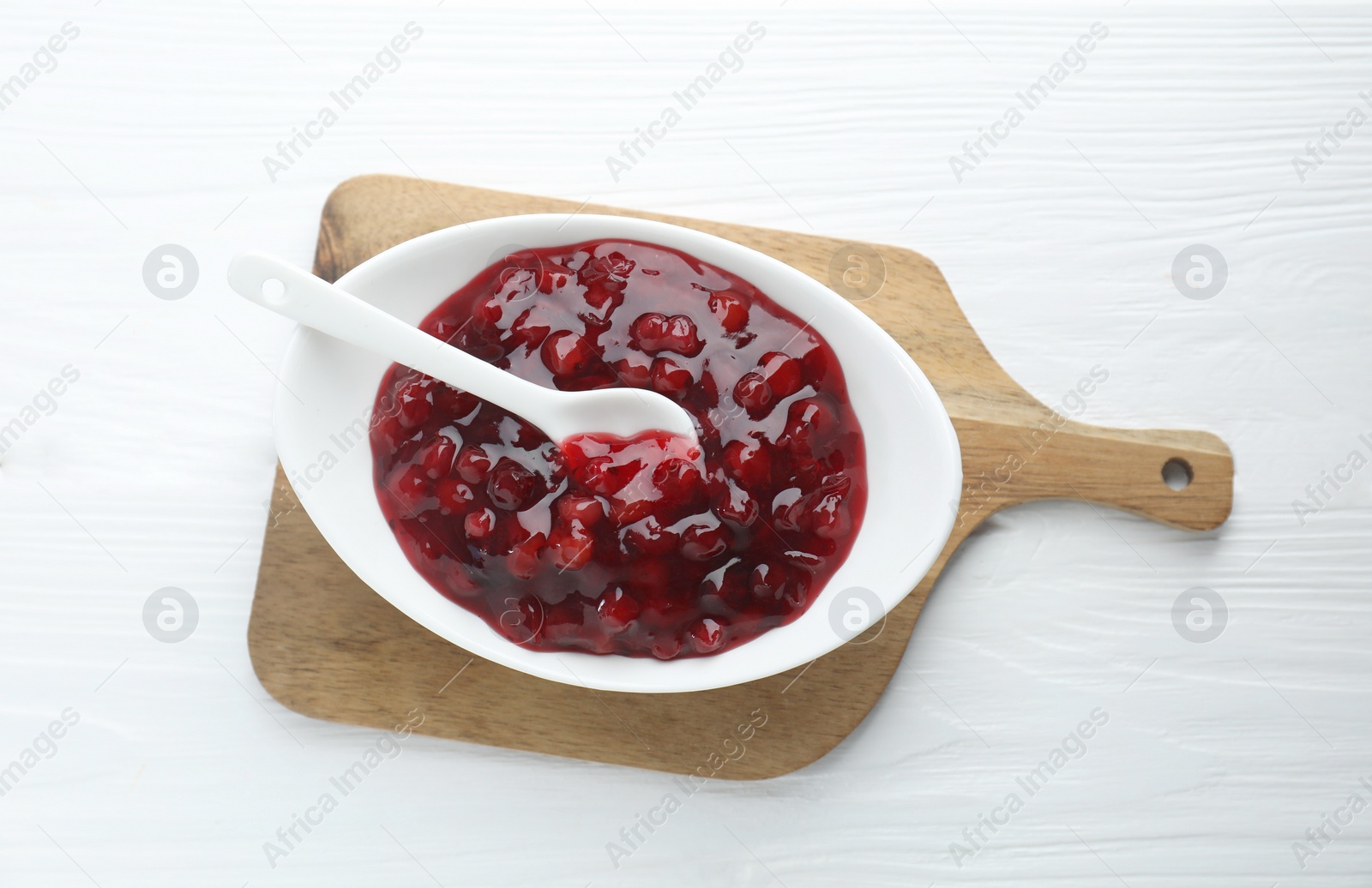 Photo of Fresh cranberry sauce in bowl and spoon on white wooden table, top view