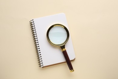 Photo of Magnifying glass and notebook on beige background, top view