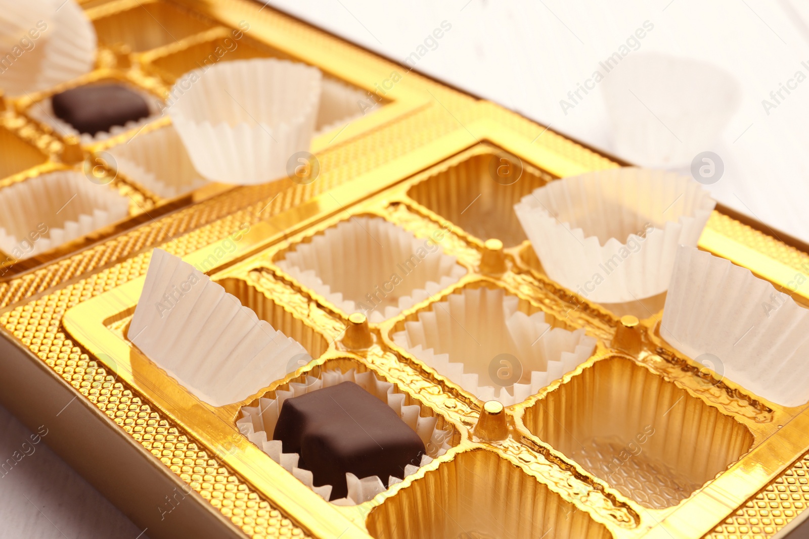 Photo of Partially empty box of chocolate candies on white wooden table, closeup