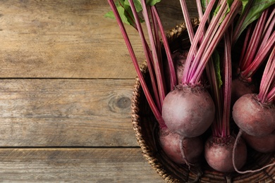 Photo of Raw ripe beets in wicker bowl on wooden table, top view. Space for text