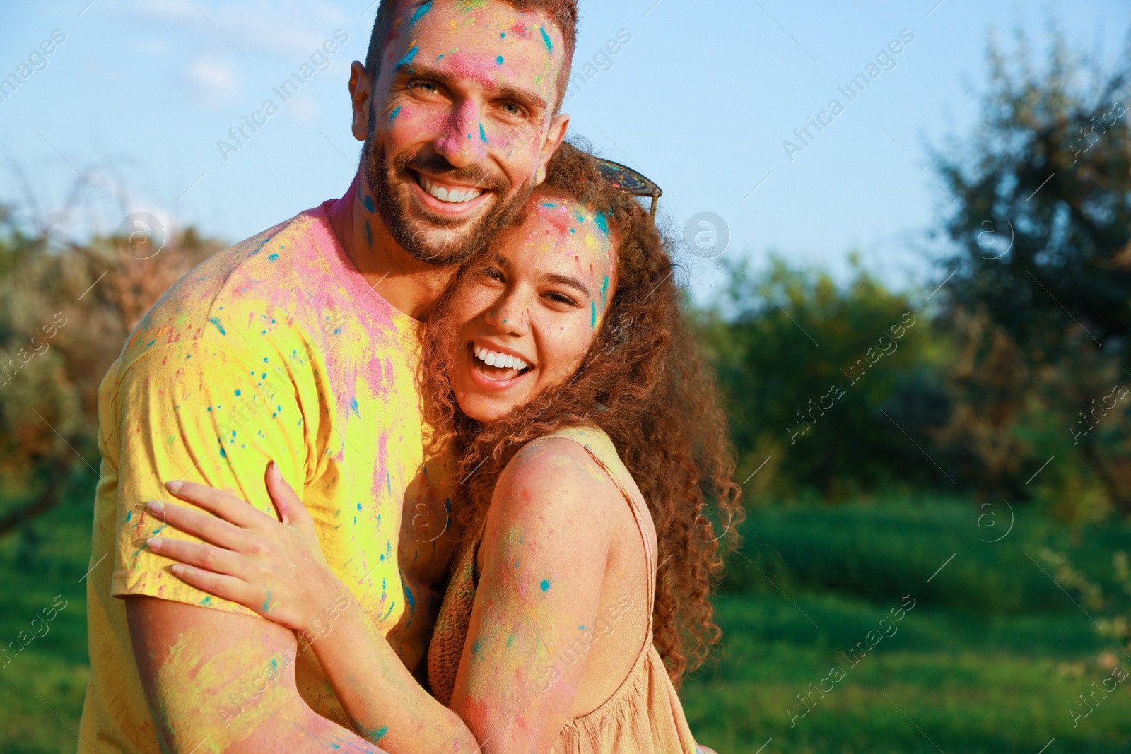 Photo of Happy couple covered with colorful powder dyes outdoors. Holi festival celebration