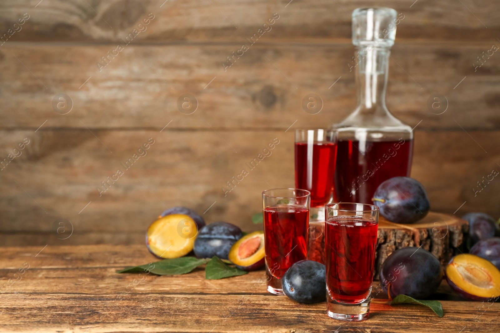 Photo of Delicious plum liquor and ripe fruits on wooden table. Homemade strong alcoholic beverage