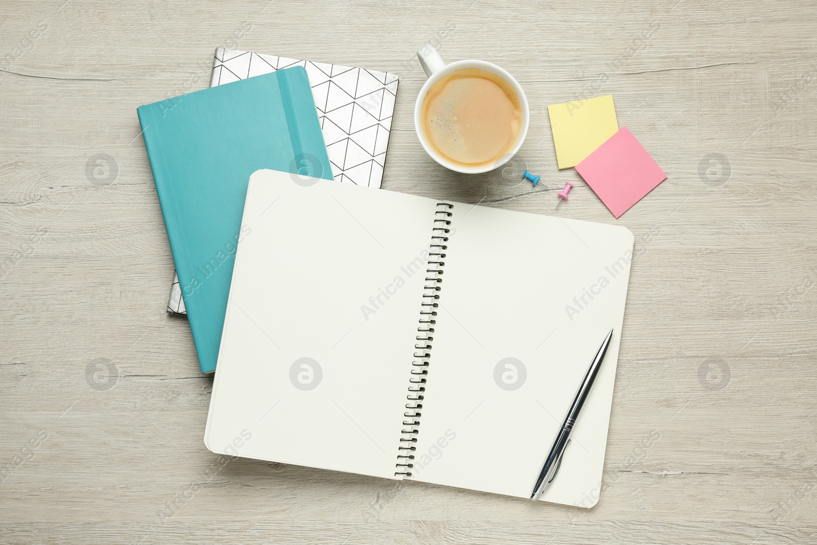 Photo of Notebooks, cup of coffee and office stationery on white wooden table, flat lay