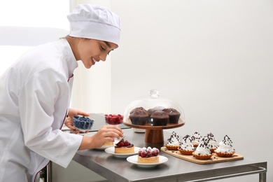 Female pastry chef decorating desserts with berries at table in kitchen