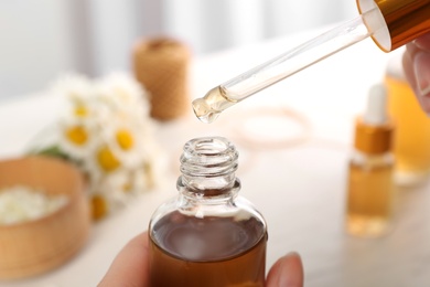 Photo of Woman holding bottle and pipette with essential oil over table, closeup