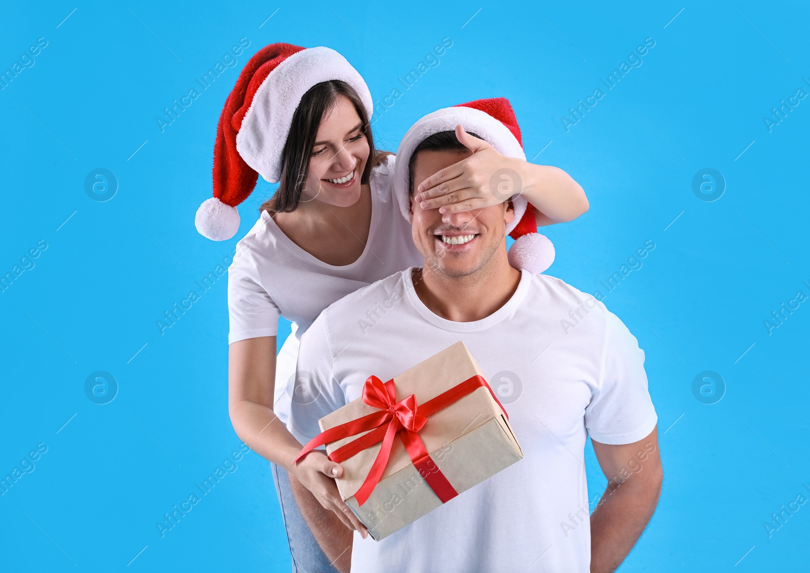 Photo of Woman presenting Christmas gift to boyfriend on light blue background