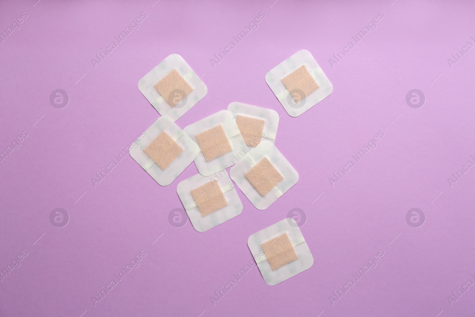 Photo of Sticking plasters on lilac background, flat lay