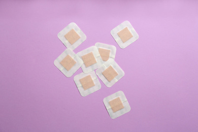 Sticking plasters on lilac background, flat lay