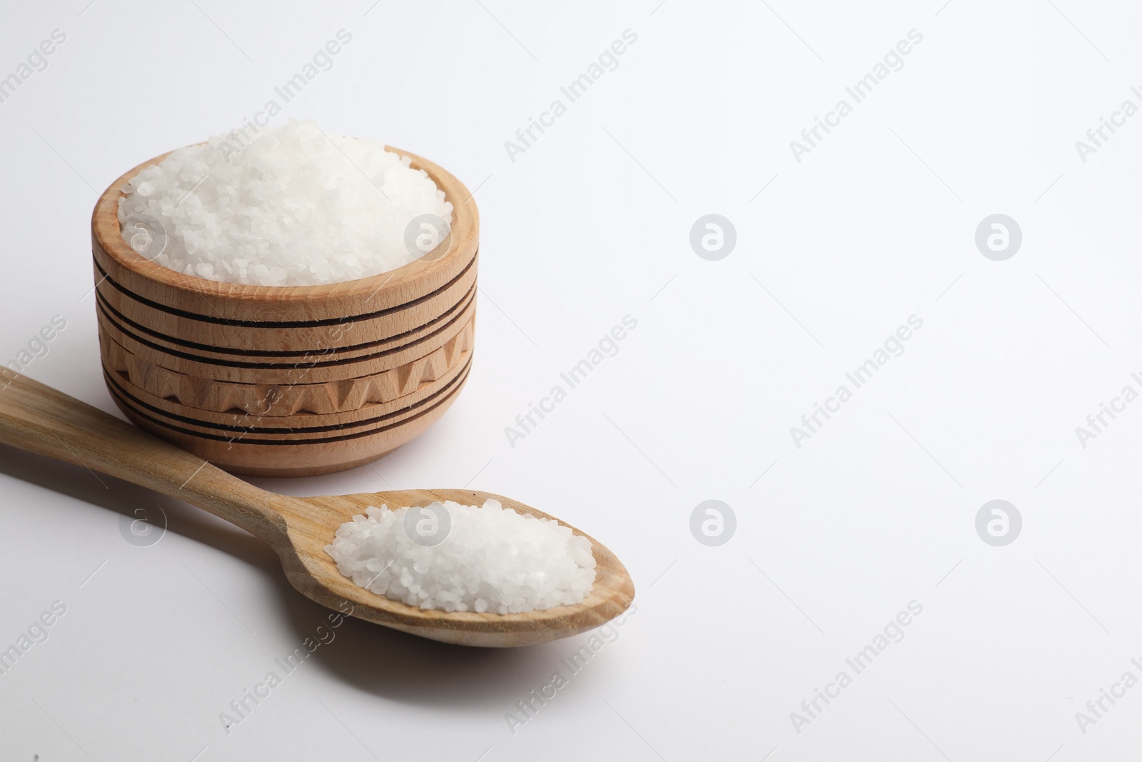 Photo of Natural salt in wooden spoon and bowl on white background, space for text