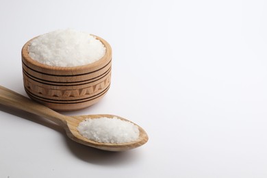 Photo of Natural salt in wooden spoon and bowl on white background, space for text