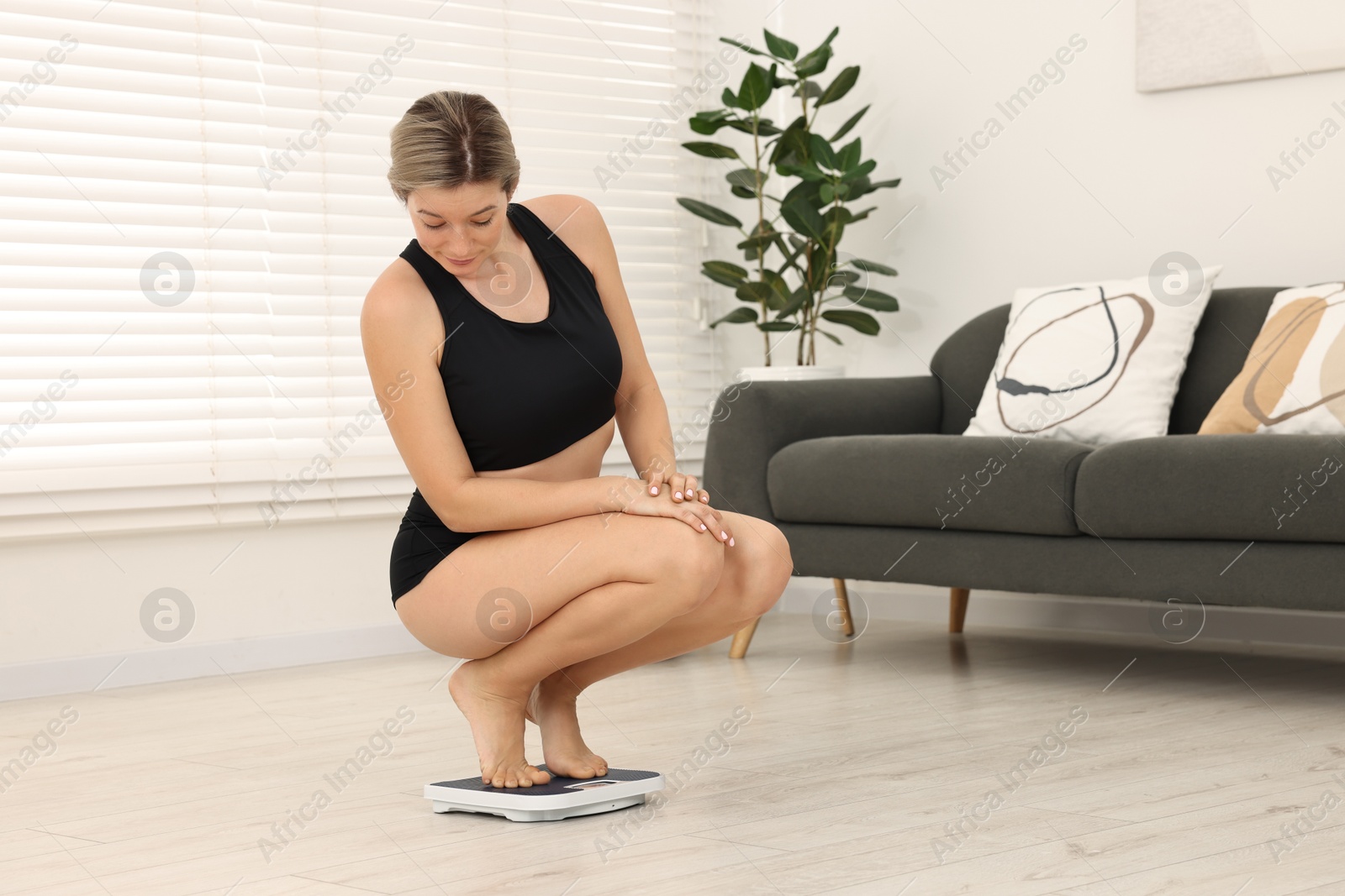 Photo of Woman in sportswear standing on floor scales at home